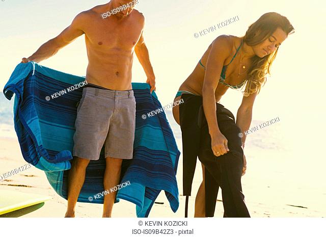 Surfing couple putting on wet suit at Newport Beach, California, USA