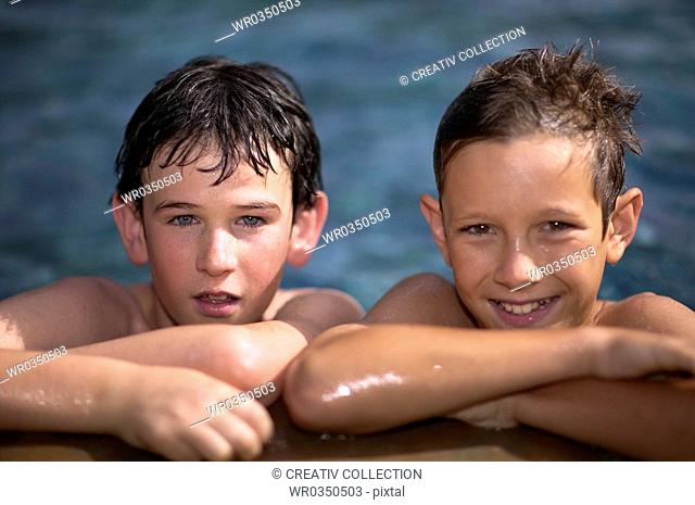 two boys resting on the edge of a swimming pool