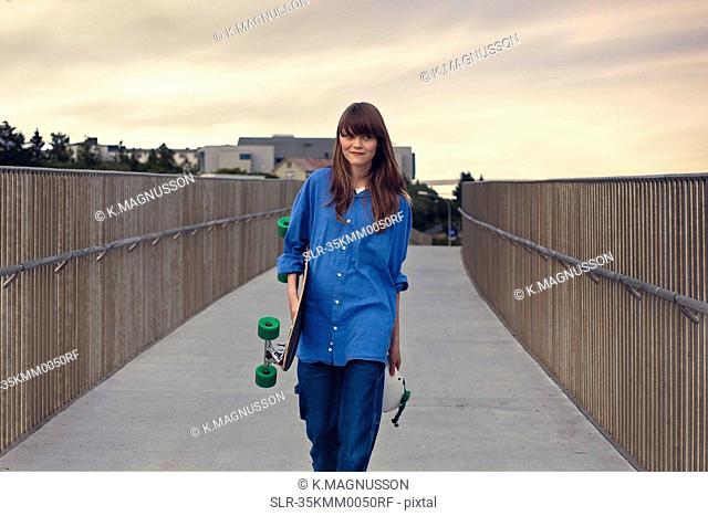 Girl carrying skateboard on walkway