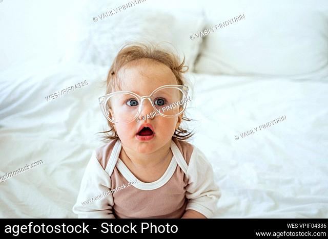 Cute girl wearing eyeglasses sitting on bed at home