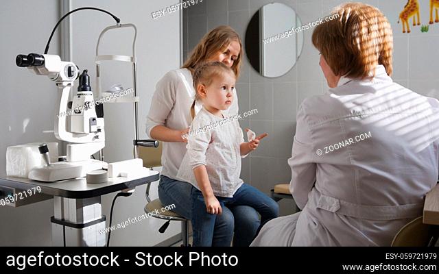 Ophthalmologist in clinic explains diagnosis about girl's eyesight - child plays, horizontal