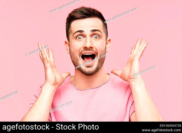 Close up portrait of surprised and amazed man with arms raised over pink background. Emotions, success, winner concept