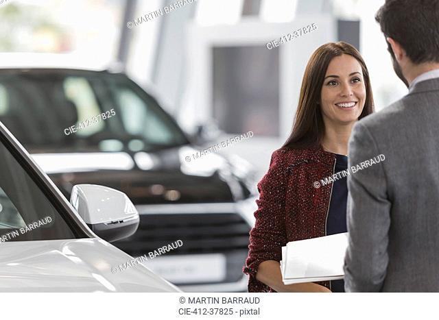 Smiling female customer listening to car salesman in car dealership showroom