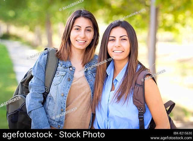 Two beautiful young ethnic twin sisters with backpacks walking outdoors