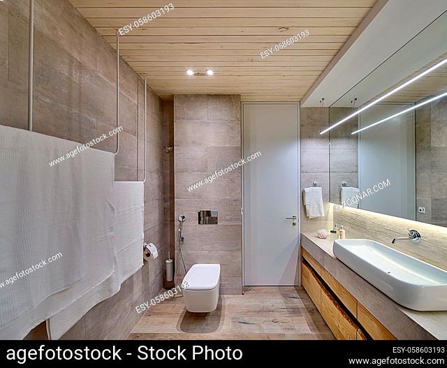 Bathroom in a modern style with textured tiles and a wooden ceiling. There is a white sink on the rack, wooden lockers, mirror, towel holders, toilet, shower