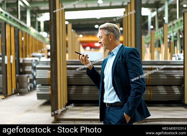 Mature businessman holding mobile phone in a factory