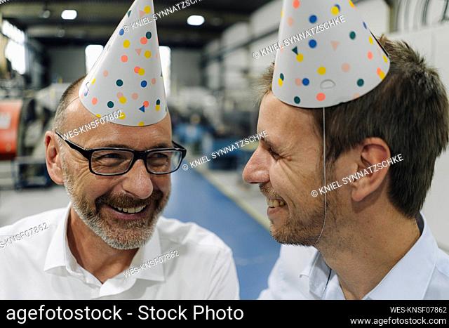 Portrait of two happy businessmen wearing party hats in a factory