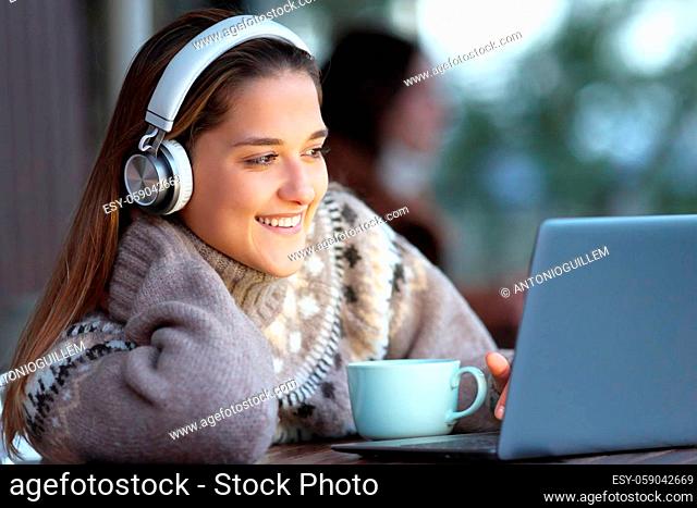 Happy woman wearing headphones watching and listening media on laptop sitting in a bar