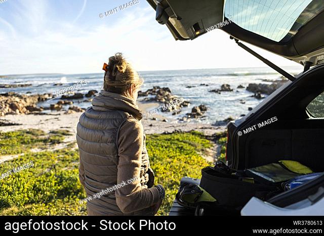Adult woman by the open door of a vehicle at the beach getting ready for hiking