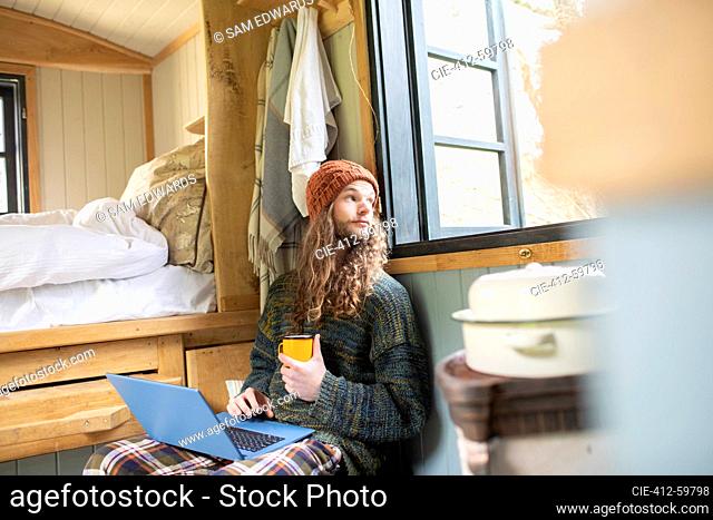 Young man with coffee using laptop in tiny cabin