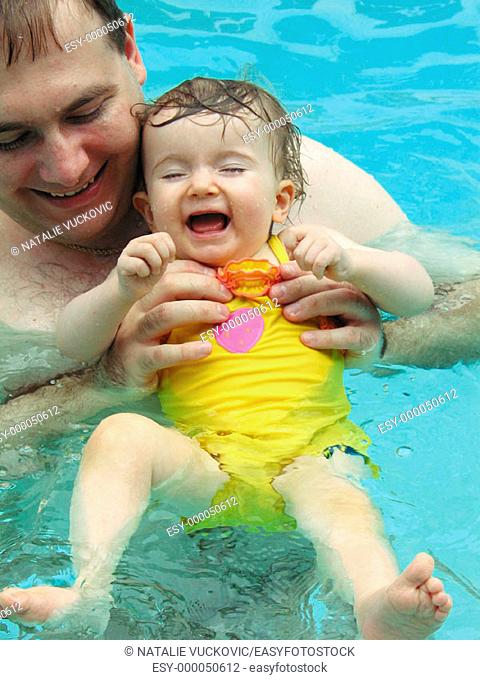 Toddler Girl splashing and laughing with daddy at the swimming pool
