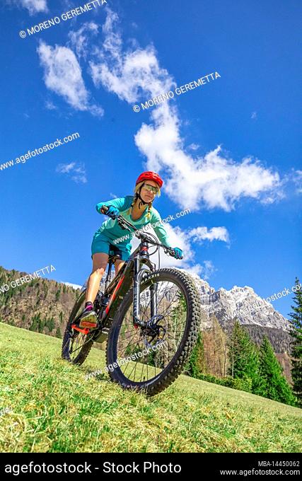 Caucasian blonde woman with sports technical clothing riding an e-bike in the mountains, dolomites, Belluno, Veneto, Italy