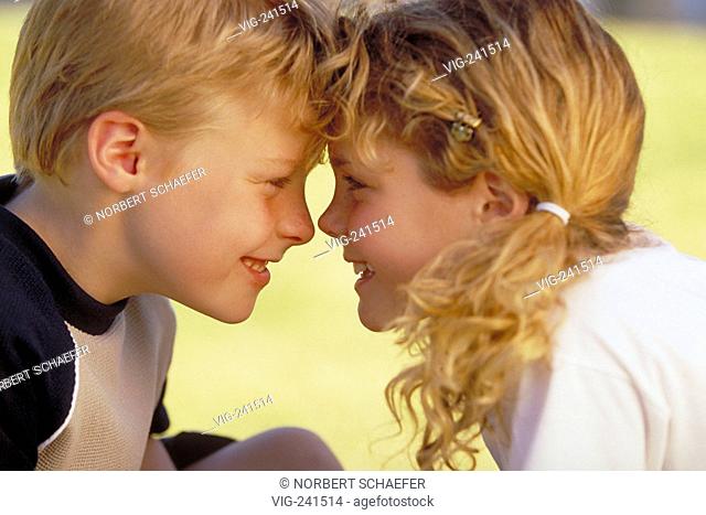 park-scene, portrait, close-up, profile, blond curly girl with plaits wearing white t-shirt and blond boy with blue-beige sweater in the age of 8 years sitting...
