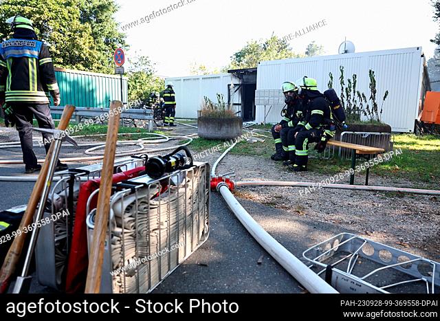 28 September 2023, Bavaria, Erlangen: Firefighters work in the smoking debris of a refugee shelter. The shelter consists of several containers