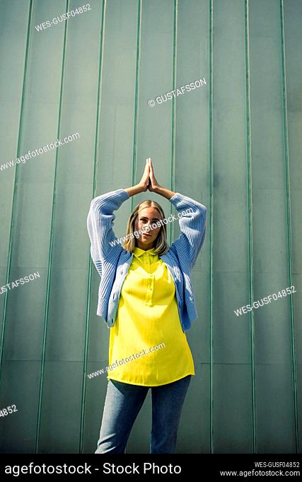 Young woman with hands clasped against wall on sunny day