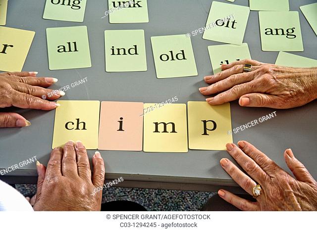 Using 'word card' components to form a complete word, a volunteer adult literacy teacher instructs an elderly Hispanic student who cannot read or write English...