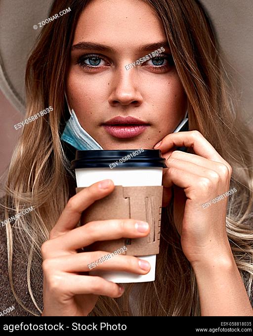 Beautiful vaccinated girl drinking coffee while pulling fown the protective face mask