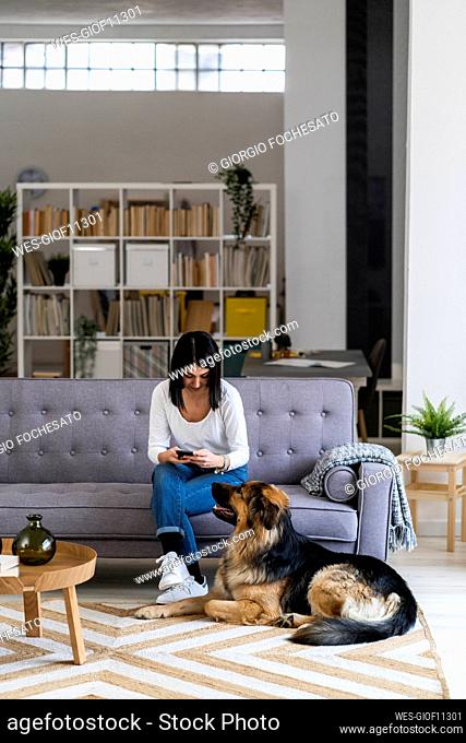 Young women using smart phone while sitting with dog in living room