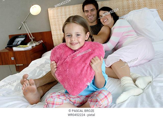 Portrait of a girl holding a stuffed pink heart with her parents lying on the bed