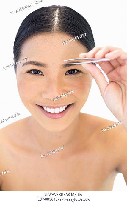 Smiling natural model using tweezers for her eyebrow