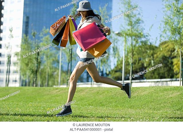 Young woman running through park, carrying several shopping bags