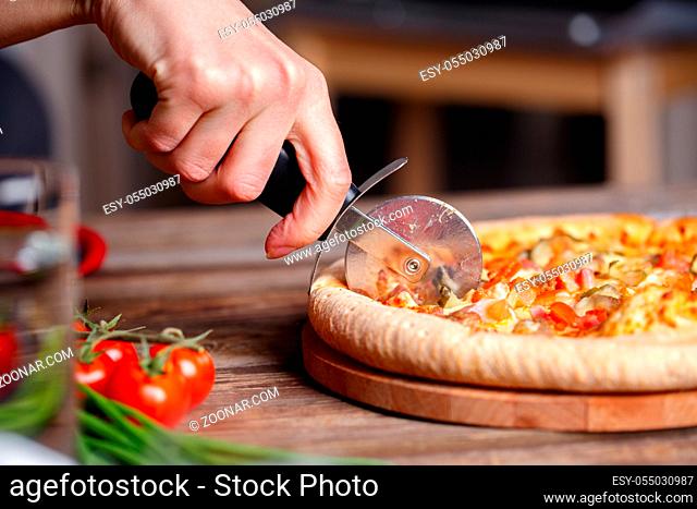 Slicing fresh pizza with pizza knife. Shallow dof. Focused on hand