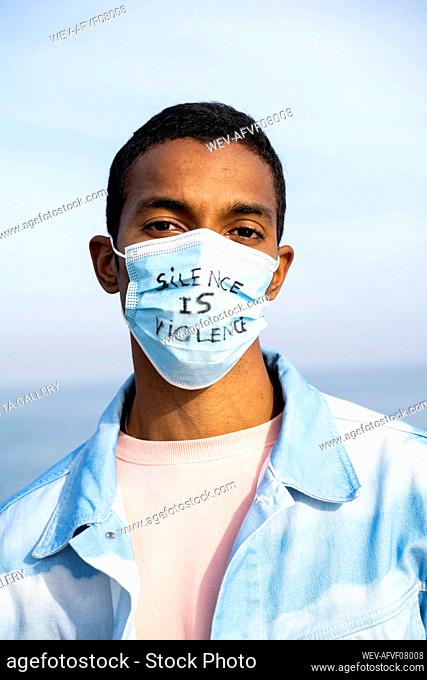 Young man wearing Silence Is Violence written face mask standing outdoors