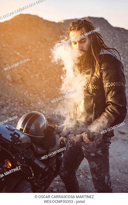 Portrait of bearded biker with dreadlocks smoking electronic cigarette