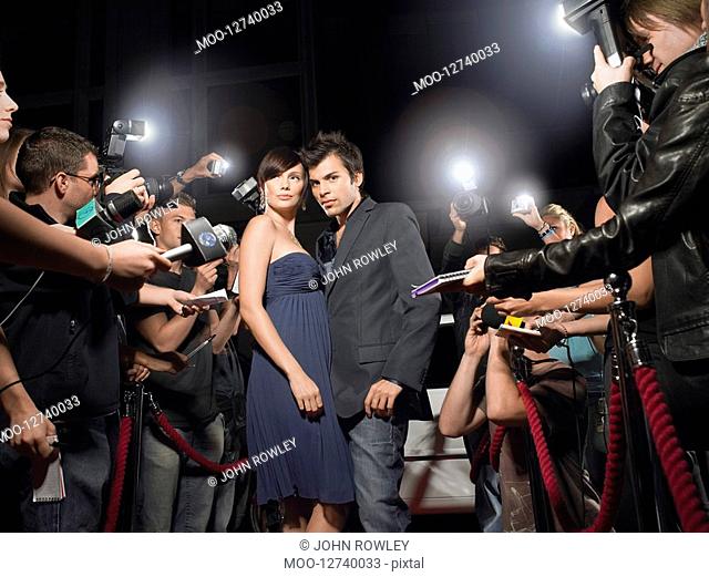 Couple posing on red carpet being photographed by paparazzi