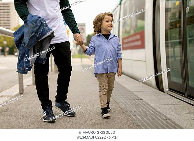 Father and son walking hand in hand at tram stop in the city
