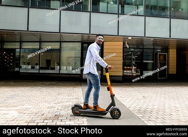 Young man riding electric push scooter on footpath