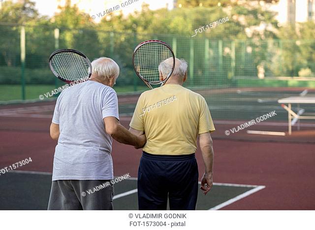 Rear view of senior friends carrying tennis rackets while walking at playing field