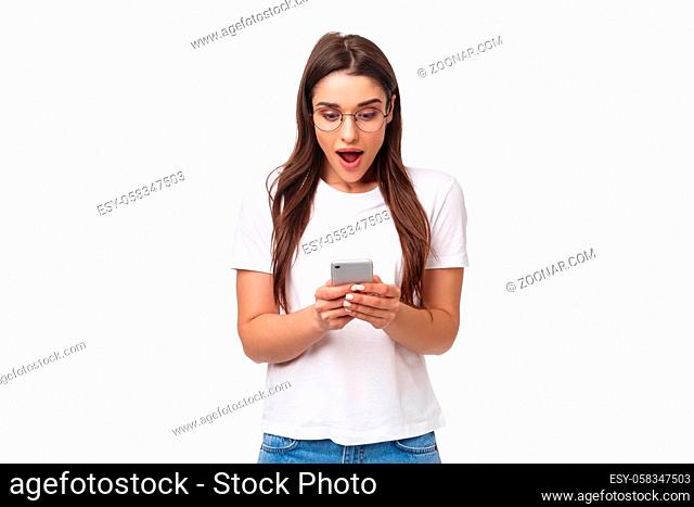 Communication, technology and lifestyle concept. Portrait of surprised and amazed, excited young caucasian woman in glasses, looking at mobile phone