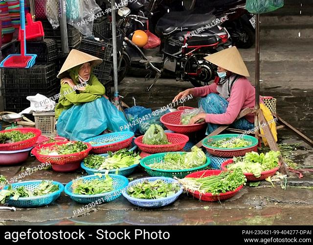 02 March 2023, Vietnam, Hoi An: Two women sit on the side of the road near the market in Hoi An selling fresh herbs and salads
