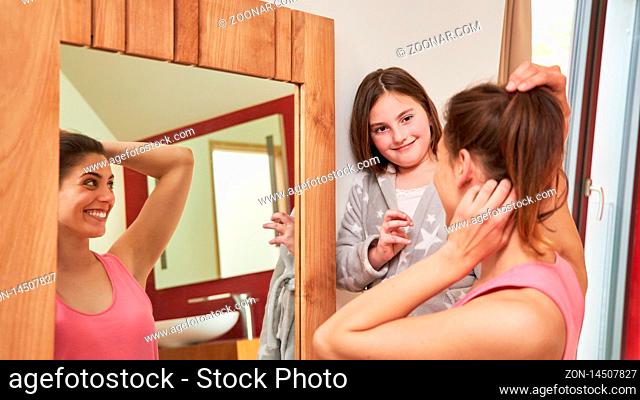 Mutter richtet sich die Frisur vor dem Spiegel mit Hilfe ihrer Tochter