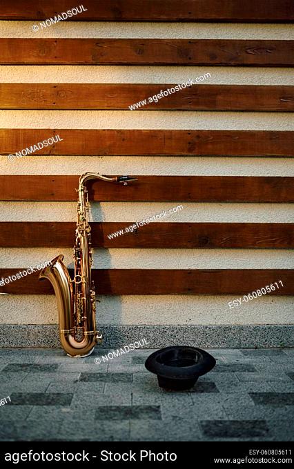 Galden saxophone and begging hat at the wall, nobody. Street musician hobby concept, urban talent. Sax outdoors, musical performance in city