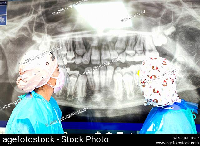 Dentist and assistant in protective workwear examining dental x-ray at office