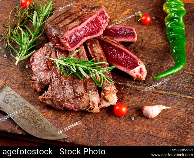 roasted piece of beef ribeye cut into pieces on a vintage brown chopping board, rare doneness. Delicious steak, top view