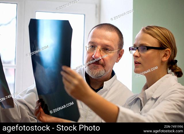 Young and experienced doctors looking at two x-ray images and trying to make a right diagnosis