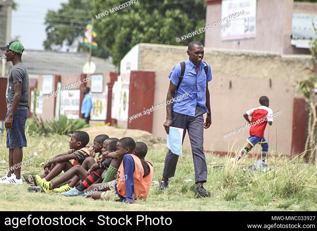 A scholar in uniform passes by as the junior academy players celebrate a goal during an u12 soccer tournament in Chitungwiza, Zimbabwe