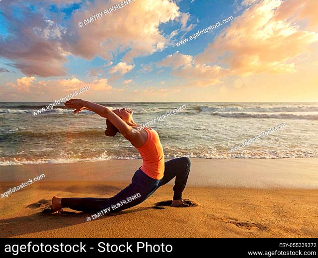 Yoga outdoors - sporty fit woman practices yoga Anjaneyasana - low crescent lunge pose outdoors at beach on sunset