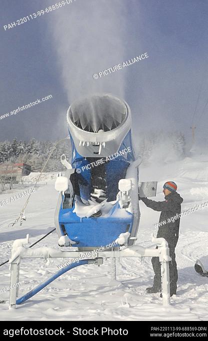 12 January 2022, Saxony, Oberwiesenthal: An employee of the Oberwiesenthal lift company adjusts a snow cannon on the slope of the Fichtelberg