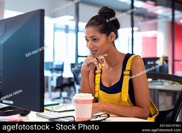 Mixed race female creative worker sitting at desk using computer