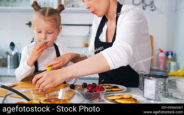 Little girl talking with her mother which cooking cottage cheese pancakes in the kitchen, close up