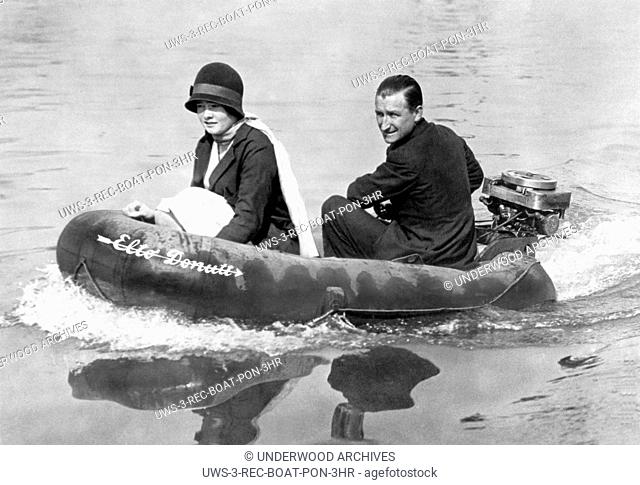 London, England: c. 1931.A happy English couple on an outing on the Thames. They are in a rubber lifesaving boat outfitted with an American outboard motor to...