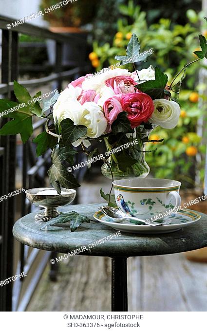 Vase of ranunculus and cup and saucer on table on balcony