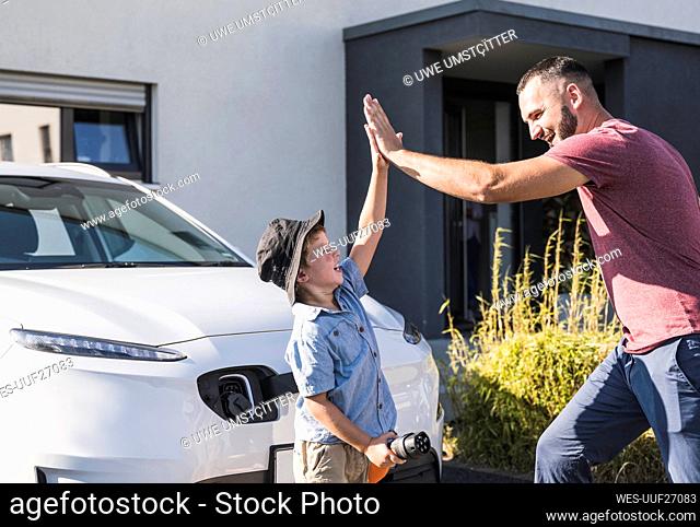 Happy father and son high fiving in front of electric car