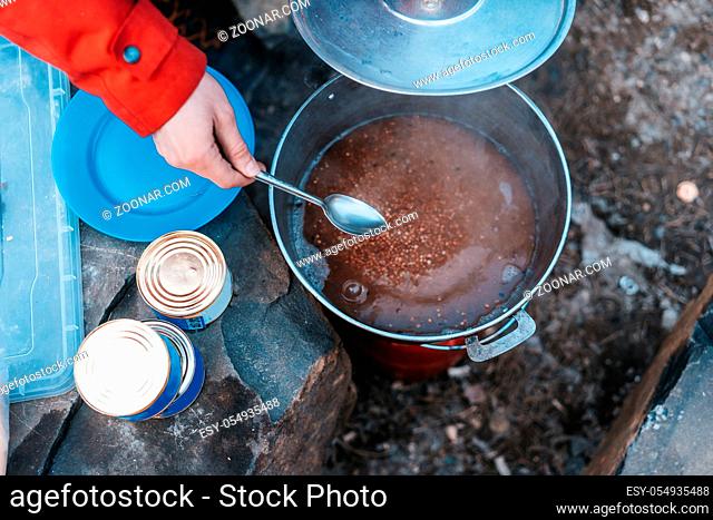 Camper preparing meal in large kettle on campfire from above