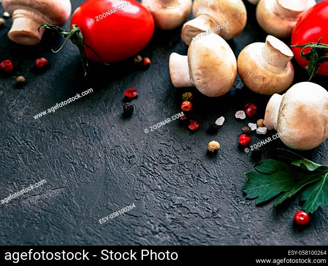 Food ingredients on black background, copy space Mini champignons, cherry tomatoes, herbs and spices top view or flat lay