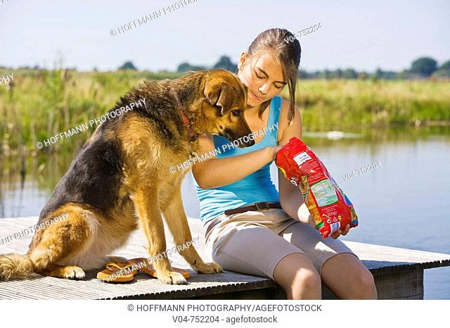 Teenaged girl and her pet dog eating potato chips outdoors at a lake